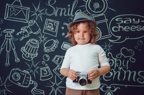 Маленький хлопчик з камерою, що стоїть на тлі чорних стін зі словами — стокове фото