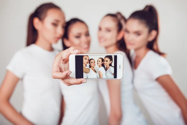 Amigos positivos retrato de quatro meninas felizes fazendo selfie, com certeza rostos engraçados, caretas, alegria, emoções, estilo casual, cores pastel, parede branca. Mulher engraçada maluca. Fundo branco . — Fotografia de Stock