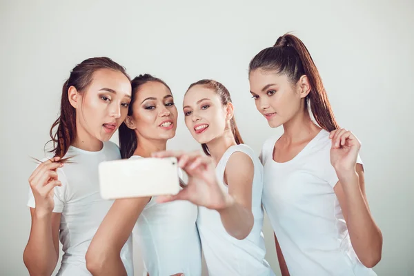 Amigos positivos retrato de cuatro chicas felices haciendo selfie, caras divertidas seguro, muecas, alegría, emociones, estilo casual, colores pastel, pared blanca. Una mujer loca y divertida. Fondo blanco . —  Fotos de Stock