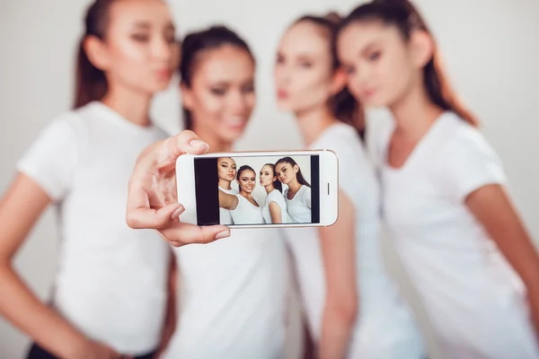 Amigos positivos retrato de cuatro chicas felices haciendo selfie, caras divertidas seguro, muecas, alegría, emociones, estilo casual, colores pastel, pared blanca. Una mujer loca y divertida. Fondo blanco . — Foto de Stock