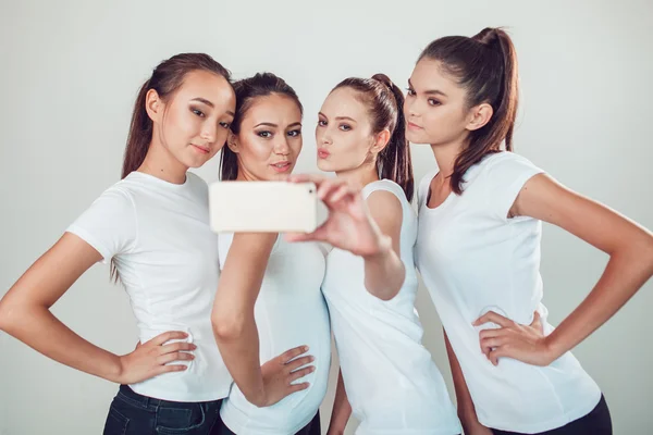 Amigos positivos retrato de cuatro chicas felices haciendo selfie, caras divertidas seguro, muecas, alegría, emociones, estilo casual, colores pastel, pared blanca. Una mujer loca y divertida. Fondo blanco . — Foto de Stock