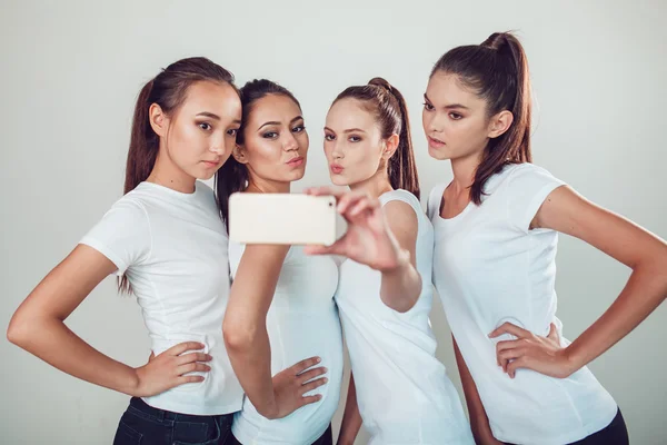 Amigos positivos retrato de cuatro chicas felices haciendo selfie, caras divertidas seguro, muecas, alegría, emociones, estilo casual, colores pastel, pared blanca. Una mujer loca y divertida. Fondo blanco . —  Fotos de Stock