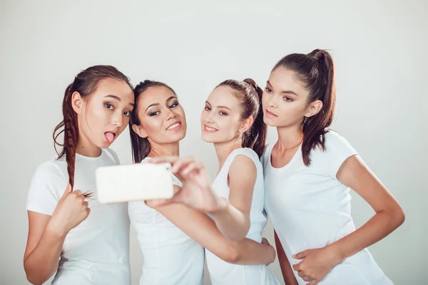 Θετική φίλοι πορτρέτο του τέσσερα κορίτσια ευτυχισμένη κάνοντας selfie, σίγουρα αστεία πρόσωπα, γκριμάτσες, χαρά, συναισθήματα, casual στυλ, παστέλ χρώματα, λευκό τοίχο. τρελή γυναίκα αστεία. Λευκό φόντο. — Φωτογραφία Αρχείου