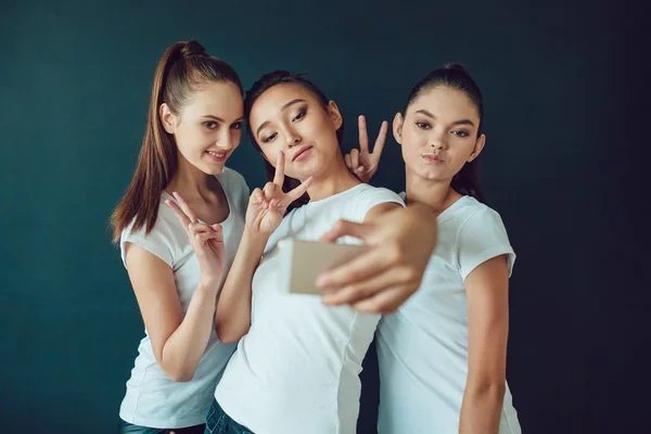 Positive friends portrait of happy girls making selfie, sure funny faces, grimaces, joy, emotions, casual style, pastel colors. Dark background. — Stock Photo, Image