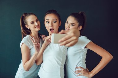 Mutlu kız yapma selfie, tabii ki komik suratlar, palyaçoluk, sevinç, duygular, rahat tarzı, pastel renkler olumlu arkadaş portresi. Koyu arka plan.