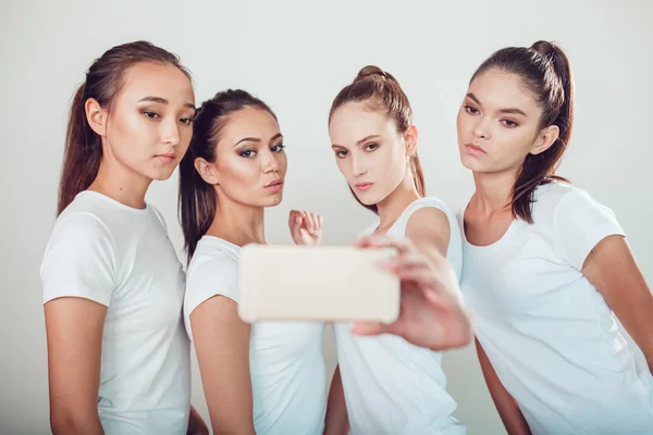 Amigos positivos retrato de cuatro chicas felices haciendo selfie, caras divertidas seguro, muecas, alegría, emociones, estilo casual, colores pastel, pared blanca. Una mujer loca y divertida. Fondo blanco . — Foto de Stock