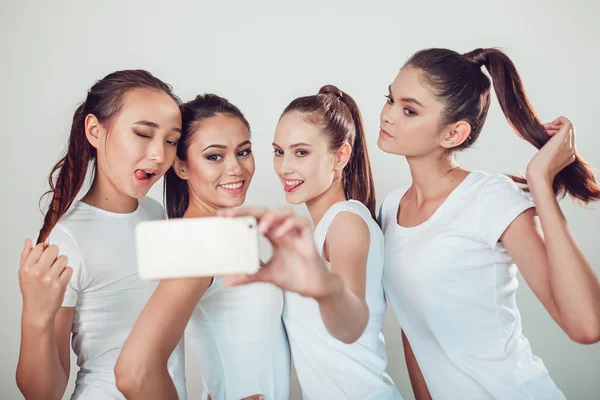 Amigos positivos retrato de quatro meninas felizes fazendo selfie, com certeza rostos engraçados, caretas, alegria, emoções, estilo casual, cores pastel, parede branca. Mulher engraçada maluca. Fundo branco . — Fotografia de Stock