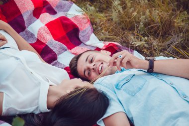 Güzel genç mutlu sevgi dolu çift üzerinde piknik ve dinlenme zevk güneşli yaz gününde ekose üzerinde uzanmış. sarılma ve birbirine bakarak ve gülümseyen.