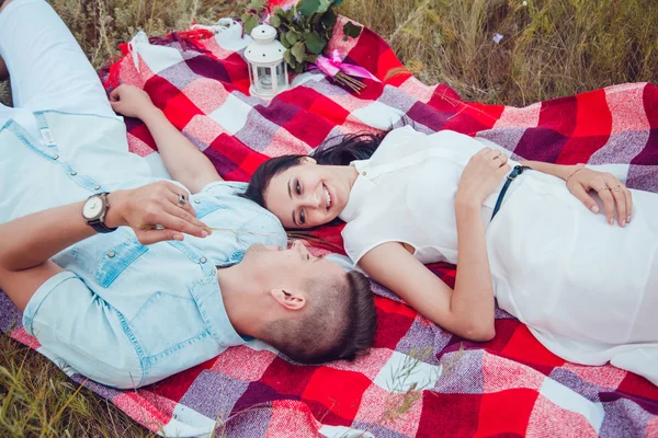 Bella giovane coppia felice amorevole sul pic-nic sdraiato sul plaid nella soleggiata giornata estiva godendo e riposando. abbracciarsi e guardarsi e sorridere . — Foto Stock