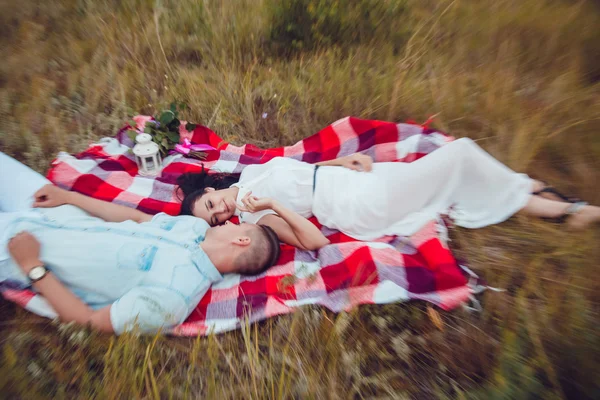 Vackra unga lyckliga älskande par på picknick liggande på Pläd solig sommar dag njuta och vila. kramas och tittar på varandra och ler. — Stockfoto