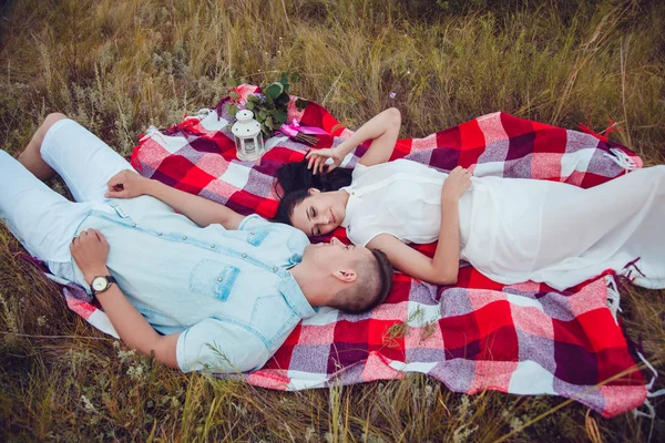 Vackra unga lyckliga älskande par på picknick liggande på Pläd solig sommar dag njuta och vila. kramas och tittar på varandra och ler. — Stockfoto