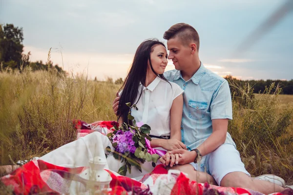 Bella giovane coppia felice amorevole sul pic-nic sdraiato sul plaid nella soleggiata giornata estiva godendo e riposando. abbracciarsi e guardarsi e sorridere . — Foto Stock