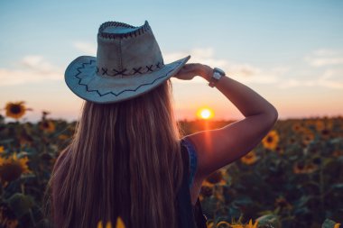 Ayçiçeği bir alanda kovboy şapkalı kız. Günbatımı