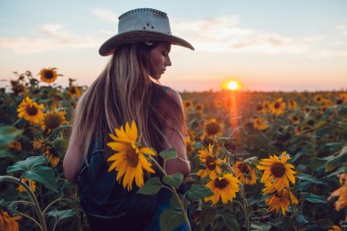 Ayçiçeği bir alanda kovboy şapkalı kız. Günbatımı
