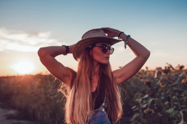 Ayçiçeği bir alanda kovboy şapkalı kız. Günbatımı