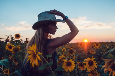 Ayçiçeği bir alanda kovboy şapkalı kız. Günbatımı