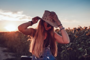 Ayçiçeği bir alanda kovboy şapkalı kız. Günbatımı