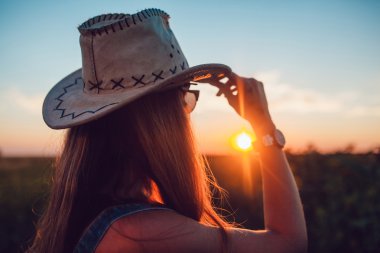 Ayçiçeği bir alanda kovboy şapkalı kız. Günbatımı