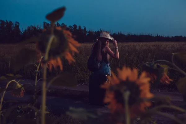 Verloren im Sonnenblumenfeld sitzt sie auf einem Koffer. Warten auf Hilfe. Nacht. — Stockfoto