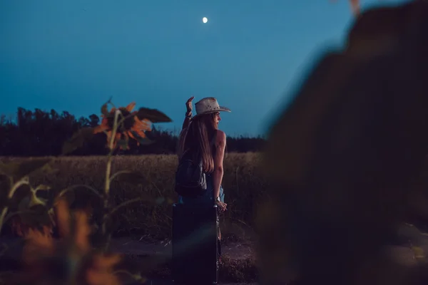 Verloren im Sonnenblumenfeld sitzt sie auf einem Koffer. Warten auf Hilfe. Nacht. — Stockfoto