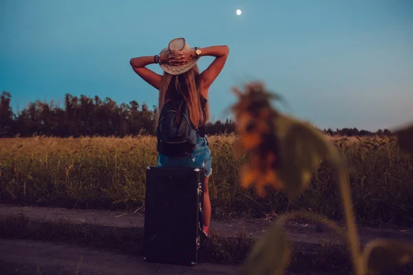 Verloren im Sonnenblumenfeld sitzt sie auf einem Koffer. Warten auf Hilfe. Nacht. — Stockfoto