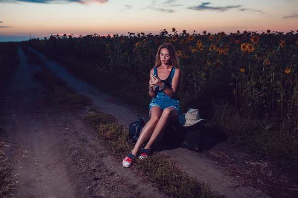 Girl sitting on a suitcase in a sunflower field. Sunset. — Stock Photo, Image