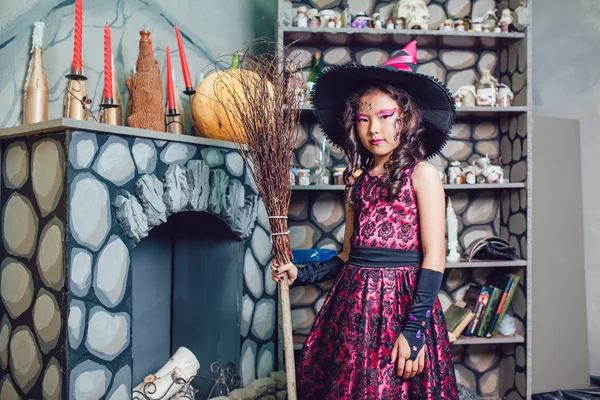 Menina em traje de bruxa de pé em decorações halloween com uma vassoura em sua mão — Fotografia de Stock