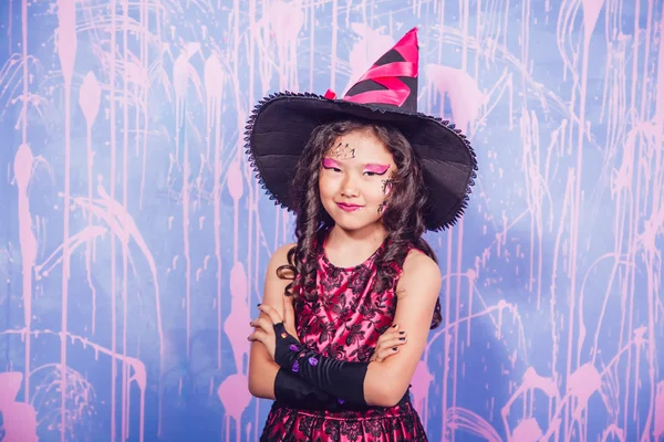 Menina em trajes de bruxa fica em um fundo roxo — Fotografia de Stock