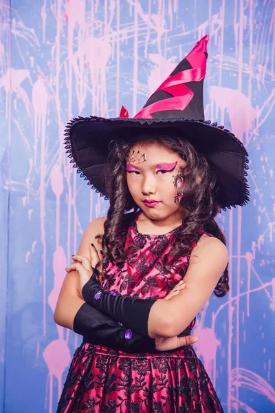 Menina em trajes de bruxa fica em um fundo roxo — Fotografia de Stock