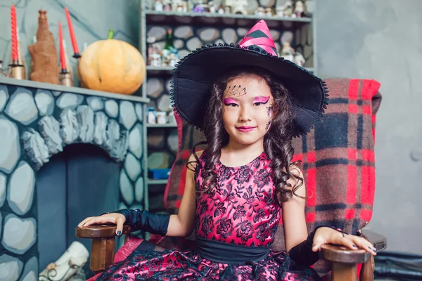 Kız Halloween süslemeleri bir sandalyede oturan bir cadı kostüm — Stok fotoğraf