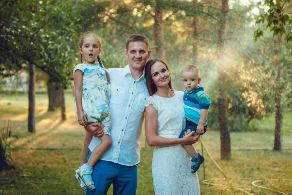 Glad ung familj på en bakgrund av vatten i parken, föräldrar håller barnen i handen — Stockfoto