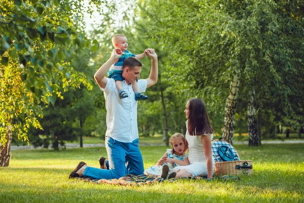 Joven familia feliz de cuatro en el picnic en el parque y el padre sosteniendo a su hijo hombros — Foto de Stock