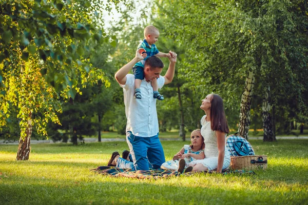 Jeune famille heureuse de quatre personnes en pique-nique dans le parc et père tenant ses épaules de fils — Photo