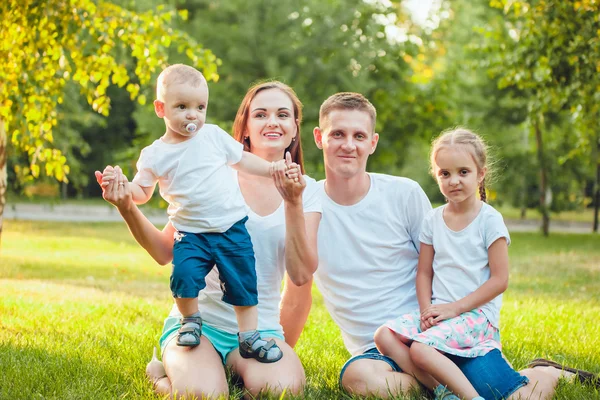 Молодая счастливая семья из четырех человек сидит в парке на траве — стоковое фото