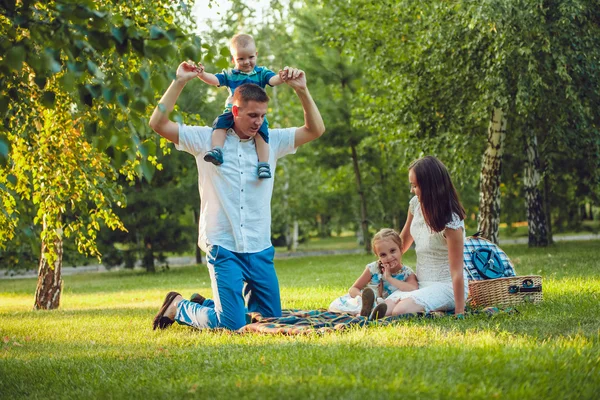 Jeune famille heureuse de quatre personnes en pique-nique dans le parc et père tenant ses épaules de fils — Photo