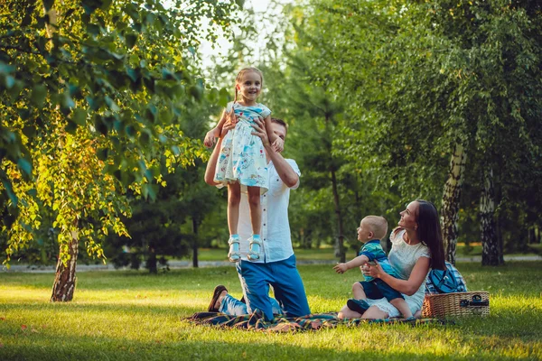 Young happy family of four on picnic in the park — Stock Photo, Image