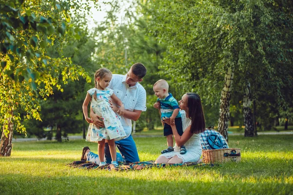 Jovem família feliz de quatro no piquenique no parque — Fotografia de Stock