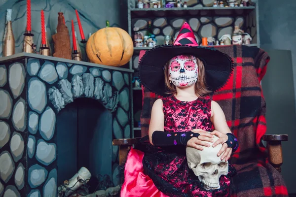 Девушка в костюме ведьмы сидит в кресле с черепом в руках в украшениях на Хэллоуин — стоковое фото