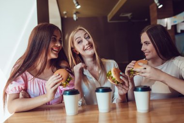 Üç neşeli genç kız bir restoranda hızlı yemek yeme