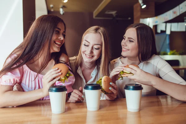 Trzy młode dziewczyny wesoły, jedzenie w restauracji fast food — Zdjęcie stockowe