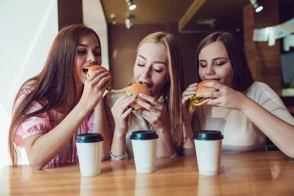 Três meninas alegres comendo fast food em um restaurante — Fotografia de Stock