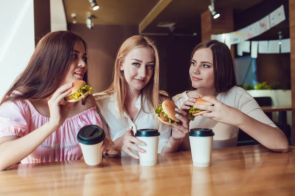 Trzy młode dziewczyny wesoły, jedzenie w restauracji fast food — Zdjęcie stockowe