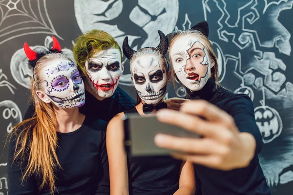 Tre ragazze e un ragazzo che vanno ad Halloween, smorfie fanno selfie — Foto Stock