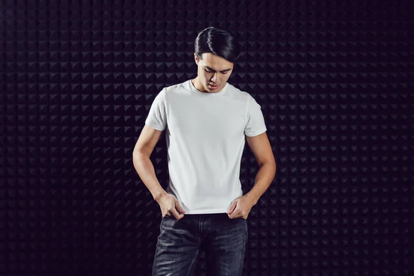 Asiatisk man i vit t-shirt på svart bakgrund. Uppställning. — Stockfoto