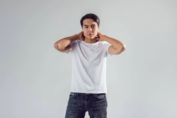 Attractive asian man in white t-shirt stands on white background. — Stock Photo, Image