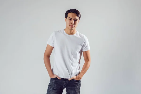 Attractive asian man in white t-shirt stands on white background. — Stock Photo, Image