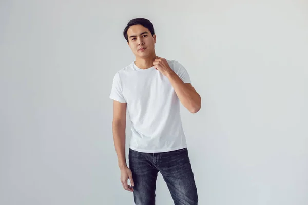 Attraktiv asiatisk man i vit t-shirt står på vit bakgrund. — Stockfoto