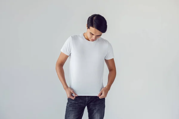 Attraktiv asiatisk man i vit t-shirt står på vit bakgrund. — Stockfoto