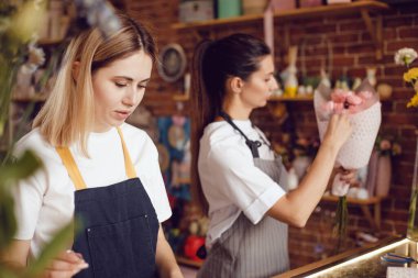 Kadın çiçekçi ve asistanı çiçekçide buket topluyor..