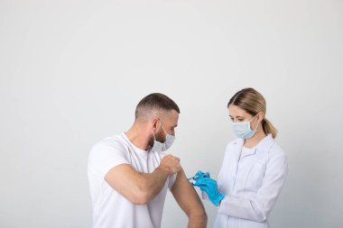 Kadın doktor, hastaya tıbbi maske takan bir adama kovid 19 aşısı enjekte ediyor..